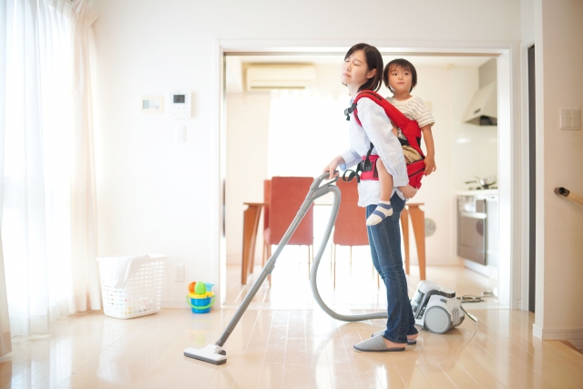 子どもを背負って、部屋の掃除機をかける女性